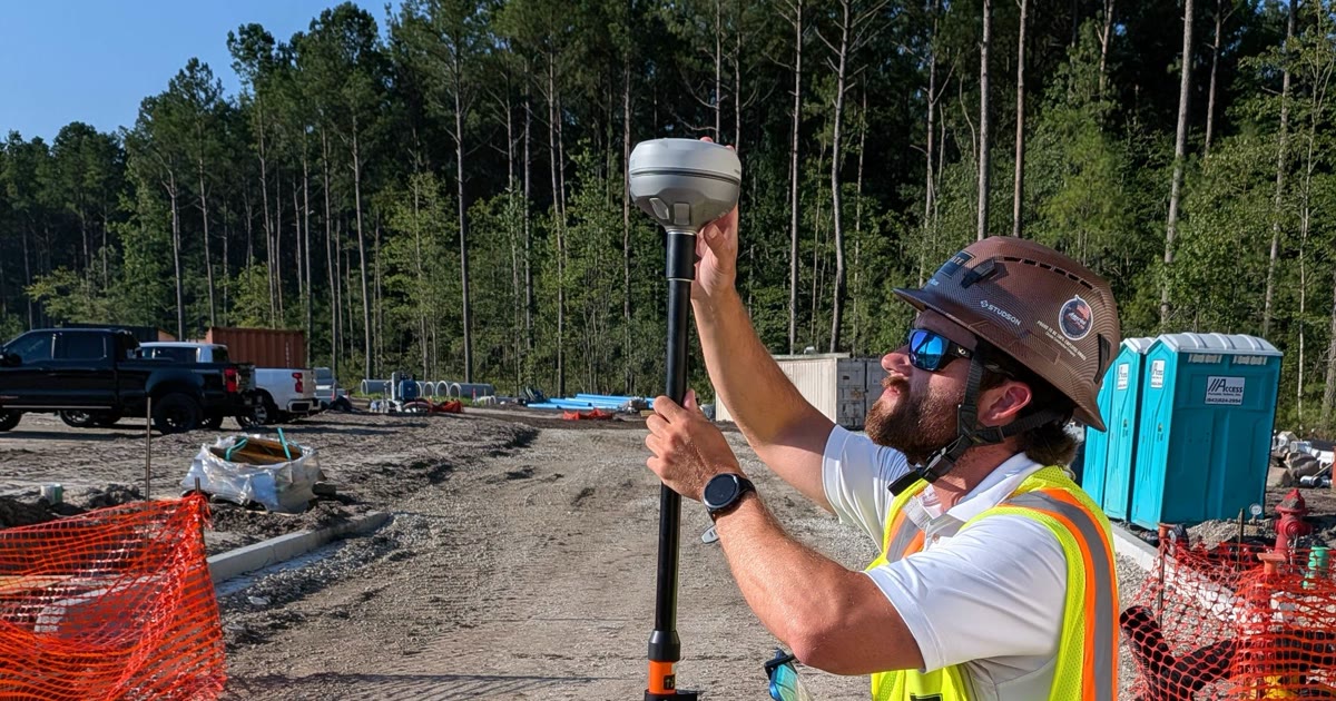 A field engineer in a hard hat holding a survey-grade GPS receiver on a construction site